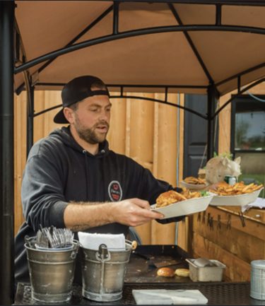 Kyle of Flossie's Sandwich Parlor plating food at an outdoor catering setup