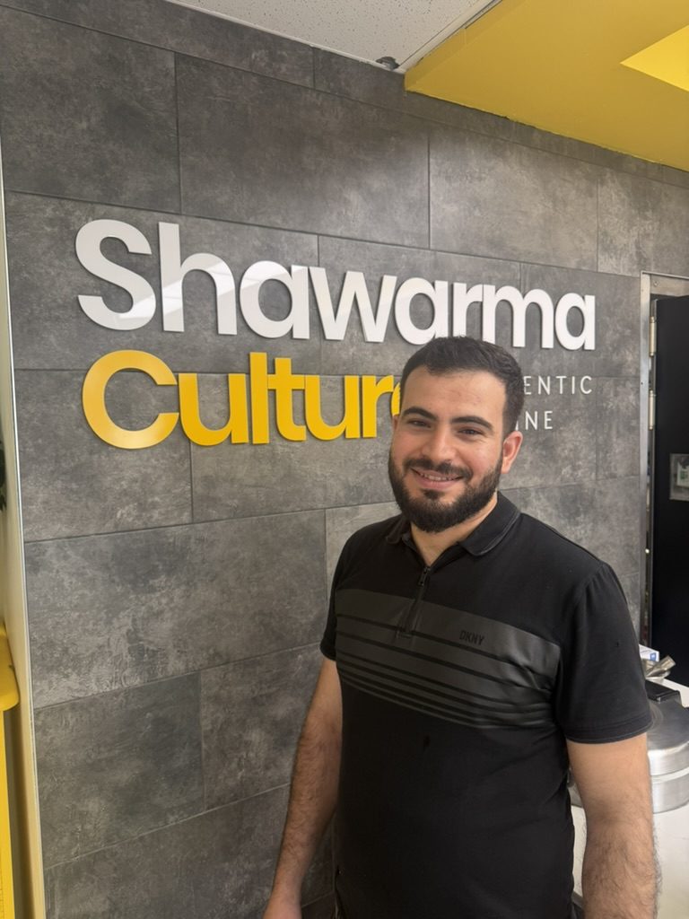 Ahmad, owner of Shawarma Culture, in front of his restaurant sign